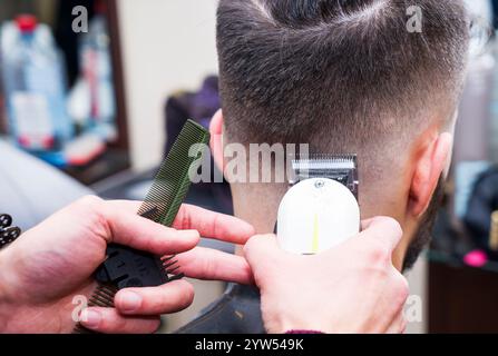 acconciatura e taglio dei capelli da uomo con il regolacapelli in un barbiere o in un parrucchiere, primo piano Foto Stock