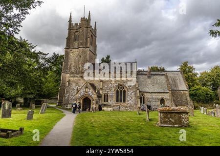 Avebury, Regno Unito - 25 agosto 2024: La chiesa di Avebury risale all'anno 1000 d.C. e si trova vicino ad Avebury Manor nel Wiltshire. una donna siede su una panchina, besi Foto Stock