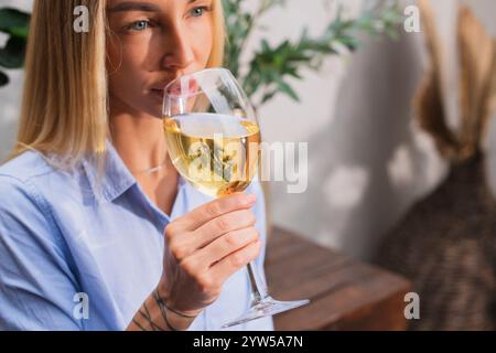 Una bella donna bionda beve vino bianco con una vetrina in mano in un'estate in giardino Foto Stock