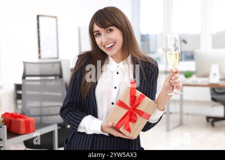 Donna felice con regalo e bicchiere di vino alla festa di Natale dell'ufficio Foto Stock