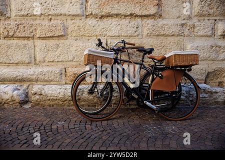 Due vecchie biciclette con cesti di vimini, utilizzate per la consegna del pane e della frutta, sono chiuse a chiave in una ringhiera in Piazza erba, Mantova, Italia, catturando il fascino Foto Stock
