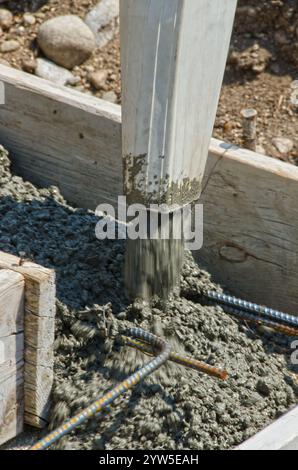 La miscela di calcestruzzo umido viene versata in forme e su tondini per creare le fondamenta di una nuova casa in costruzione. Foto Stock