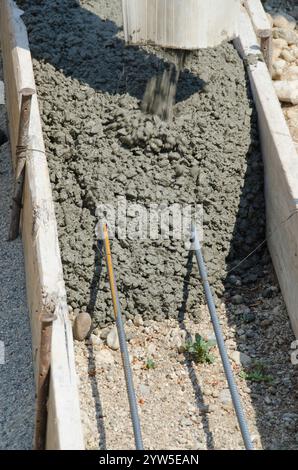 La miscela di calcestruzzo umido viene versata in forme e su tondini per creare le fondamenta di una nuova casa in costruzione. Foto Stock