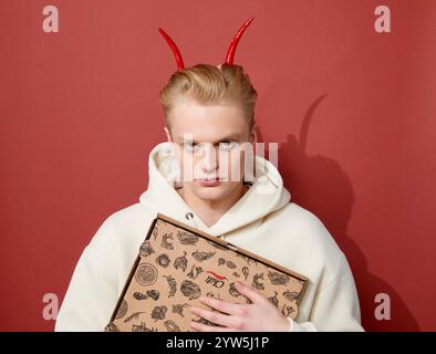 ritratto di un giovane uomo biondo in un maglione bianco con corna di pepe rosso Foto Stock