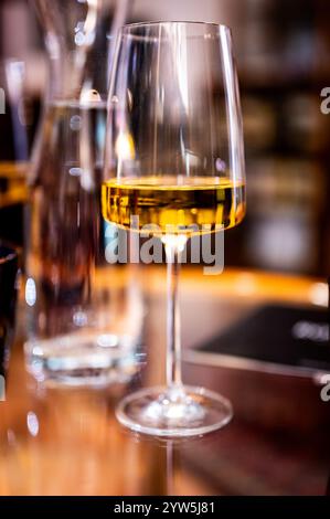 Uno shot ravvicinato di un tavolo con un bicchiere di vino moderno riempito di vino bianco, catturando l'eleganza del bicchiere e l'atmosfera raffinata del set Foto Stock