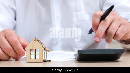 Uomo che calcola il pagamento di mutui ipotecari, l'assicurazione o l'imposta sulla proprietà sul primo piano della calcolatrice. Rifinanziamento del prestito per la casa Foto Stock