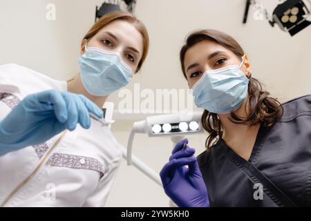 Dal basso dentisti con specchio e dispositivo piegato sopra la paziente durante l'appuntamento in clinica odontoiatrica. Foto Stock