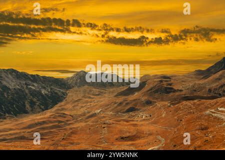 Tramonto dorato su un maestoso paesaggio di montagna con un cielo spettacolare e terreno roccioso. Foto Stock