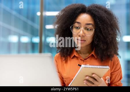 Donna sicura di sé in ufficio, che scrive attentamente appunti su un blocco note. Ideale per temi di professionalità, concentrazione e business. Perfetto per ambienti di lavoro e presentazioni aziendali. Foto Stock