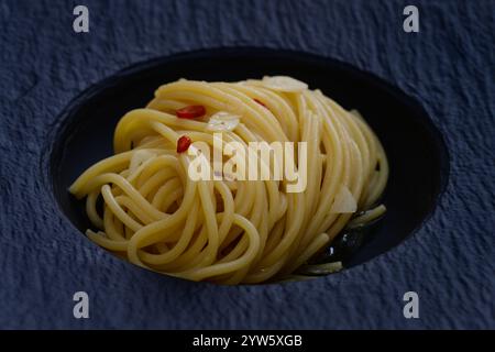 Spaghetti Colatura di Alici con aglio e peperoncini su un piatto nero da vicino Foto Stock