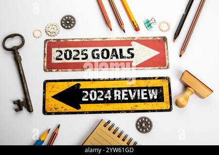 2025 obiettivi e 2024 revisione. Due frecce direzionali su una scrivania da ufficio bianca. Foto Stock
