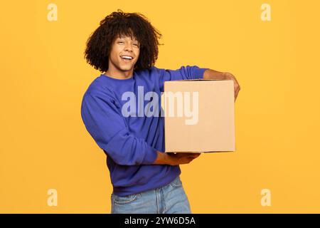 Un giovane nero con i capelli ricci sorride mentre tiene in mano una scatola di cartone Foto Stock