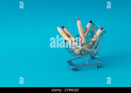 Pastelli di cera colorati nel carrello della spesa su sfondo blu. Concetto scolastico minimale. Foto Stock