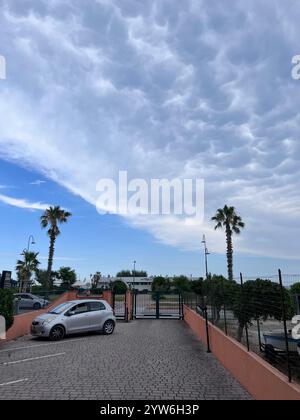 Porto Sant'Elpidio, Italia - 06 luglio 2022: Un'auto d'argento parcheggiata su un vialetto di ciottoli sotto un cielo nuvoloso, fiancheggiata da palme. Il tra Foto Stock