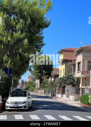 Porto Sant'Elpidio, Italia - 06 luglio 2022: Tranquilla strada suburbana con auto bianca parcheggiata, verde vivace e affascinanti case residenziali unde Foto Stock