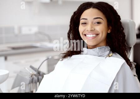 Trattamento stomatologico. Donna afroamericana sorridente seduta nella sedia dei dentisti in clinica Foto Stock