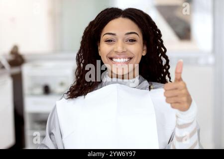 Sorridente femmina nera che sorride e mostra il pollice su dopo il trattamento dentale Foto Stock