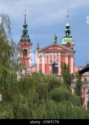 Lubiana, Slovenia - 28 giugno 2024: Storica chiesa francescana rossa e rosa dell'Annunciazione facciata monumentale con statua. Foto Stock