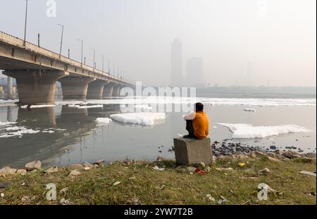 Uomo isolato che guarda la schiuma tossica nel fiume contaminato con il ponte vicino a Foggy City al mattino l'immagine viene scattata presso il fiume yamuna, la diga di okhla, delhi ind Foto Stock