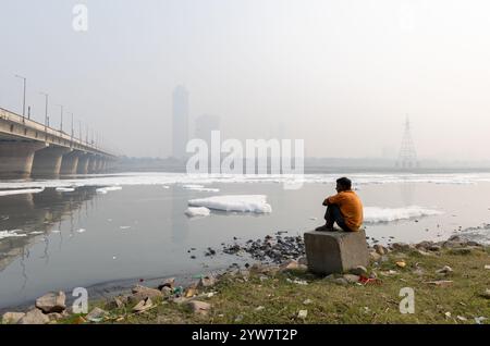 Uomo isolato che guarda la schiuma tossica nel fiume contaminato con il ponte vicino a Foggy City al mattino l'immagine viene scattata presso il fiume yamuna, la diga di okhla, delhi ind Foto Stock