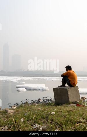 Uomo isolato che guarda la schiuma tossica nel fiume contaminato con il ponte vicino a Foggy City al mattino l'immagine viene scattata presso il fiume yamuna, la diga di okhla, delhi ind Foto Stock