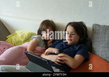 Due sorelle sdraiate sul divano che guardano la tavoletta. Concetto di bambini che trascorrono del tempo a casa Foto Stock