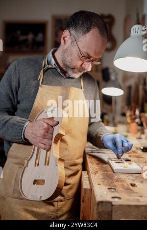 Cremona, Italia - 9 dicembre 2024 - Luca tenore maestro artigiano esperto che lavora meticolosamente su un violino nella sua bottega, dimostrando la cr tradizionale Foto Stock