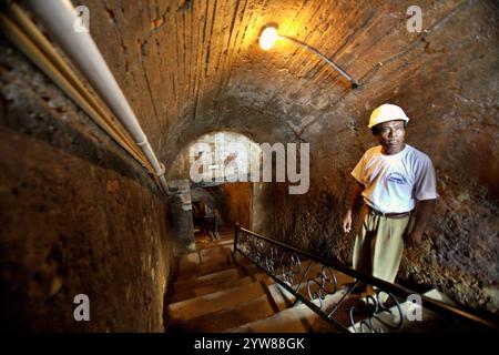 Ritratto di Wilizon, una guida, mentre è in piedi sulle scale che conducono giù al tunnel sotterraneo di estrazione del carbone a Sawahlunto, un'ex città mineraria del carbone fondata dai colonialisti olandesi alla fine del 19th secolo a Sumatra Occidentale, Indonesia. Foto Stock