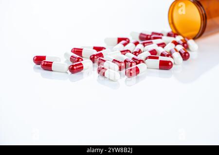 Capsule di prescrizione rosse e bianche che fuoriescono da un contenitore di plastica. Farmaci farmaceutici regolamentati. Enfatizzare gli standard di sicurezza, i farmaci Foto Stock