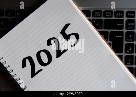 "2025" scritto a mano su un notebook posizionato su una tastiera del notebook, simboleggia un nuovo inizio di attività. Foto Stock
