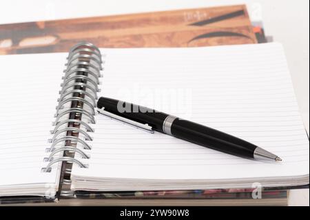 Una penna nera si trova su una pagina bianca di un notebook con rilegatura a spirale. La penna è posizionata sulla pagina e non è in uso Foto Stock