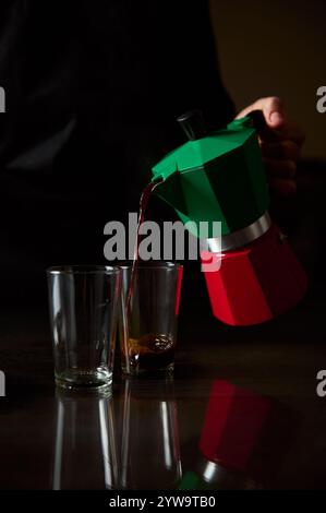 Vista ravvicinata del caffè versato da una moka verde in tazze di vetro, catturando l'aroma ricco e il calore del caffè appena estratto. Foto Stock