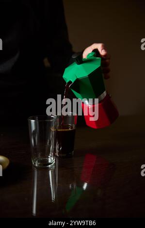 Primo piano del caffè versato da una moka in un bicchiere. La scena è calda e invitante, sottolineando il piacere del caffè appena preparato in un Foto Stock