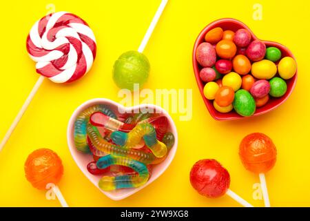 Diversi tipi di caramelle su sfondo giallo, spazio di copia. Sfondo colorato per la festa di compleanno. Foto Stock