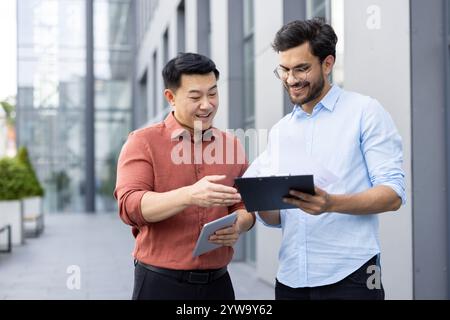 Due professionisti stanno esaminando i documenti mentre si trovano all'aperto in un ambiente urbano contemporaneo. Sembrano coinvolti e collaborativi, evidenziando il lavoro di squadra e la comunicazione in un'azienda Foto Stock