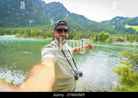 Turista con fotocamera d'epoca che scatta un selfie con i pollici sul lago di dobbiaco nelle dolomiti italiane durante le vacanze estive Foto Stock