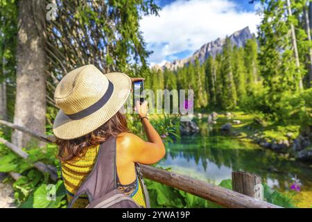 Donna turistica che scatta foto mozzafiato del lago carezza con il monte latemar riflesso nelle sue acque color smeraldo Foto Stock