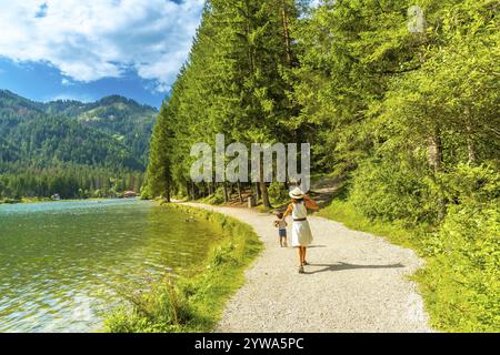 I turisti si godono una passeggiata lungo le sponde panoramiche del lago di dobbiaco, circondati dallo splendido paesaggio montano delle dolomiti in estate Foto Stock