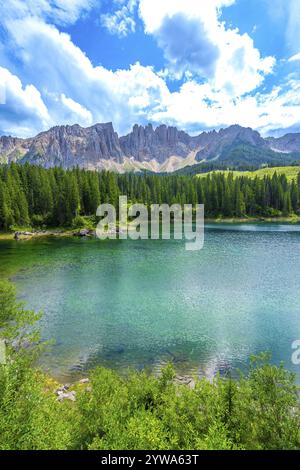 Le acque smeraldo del lago carezza riflettono la catena montuosa del latemar, circondate da una lussureggiante pineta sotto un cielo estivo nuvoloso nelle dolomiti Foto Stock