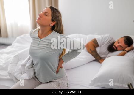 Una giovane coppia sta dormendo a letto. La donna si sta svegliando per lavoro. Ha mal di schiena. Foto Stock