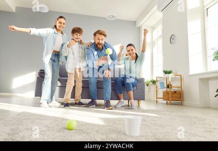 Famiglia felice a casa, madre e padre con due bambini che giocano a tennis nel soggiorno Foto Stock