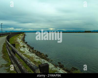 Una stretta strada curva che attraversa la laguna di Venezia, su un argine erboso, al crepuscolo, Chioggia, zona di Venezia, Italia Foto Stock