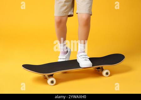 Bambina con skateboard su sfondo giallo, primo piano Foto Stock