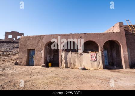 Un edificio fatto di cemento e fango con quattro archi nel mezzo del deserto marocchino. Ci sono tessuti appesi a una corda per bloccare il sole e cl Foto Stock