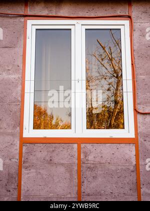 Finestra di una casa residenziale con parete di tufo rosa nella città di Erevan il giorno d'autunno Foto Stock