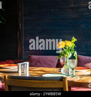 rose gialle fresche in vaso di vetro illuminato dalla luce del sole sul tavolo del ristorante Foto Stock