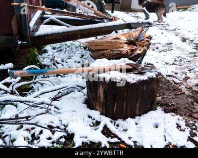 L'ascia giace su un ceppo di legno con una pila di legna da ardere tritata sul terreno innevato. Riscaldare la casa con il legno. Villaggio in Transcarpathia Ukra Foto Stock