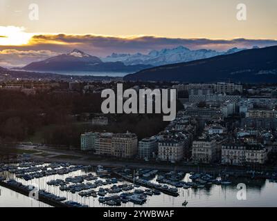 L'alba panoramica mozzafiato sulla città di Ginevra con il lago di Ginevra, le barche ormeggiate, gli edifici e le montagne innevate delle Alpi sullo sfondo Foto Stock
