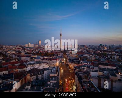 La torre della televisione di Berlino, un punto di riferimento suggestivo, si erge sul paesaggio urbano al crepuscolo, illuminando lo skyline urbano con un caldo bagliore da una vista aerea Foto Stock