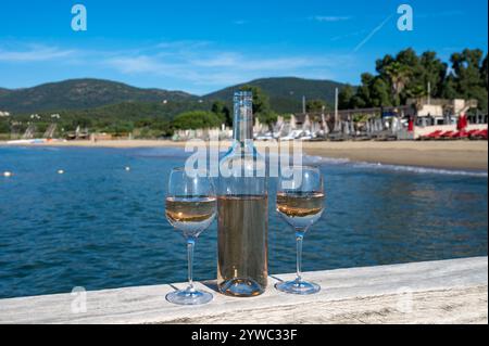 Bottiglia e bicchiere di vino di rosa freddo della Provenza e molo boota di yacht in legno sulla spiaggia di sabbia bianca Plage de Pampelonne vicino a Saint-Tropez, vacanze estive Foto Stock